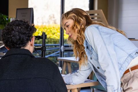 Coworkers collaborating at sunlit desk by window, woman pointing at documents