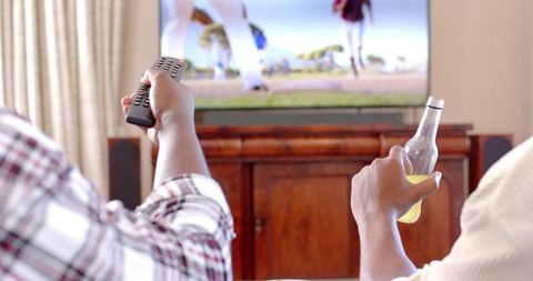 Friends watching tv together holding remote and beer bottle