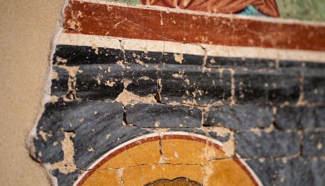Weathered fresco with cracked plaster, black band and ochre medallion detail