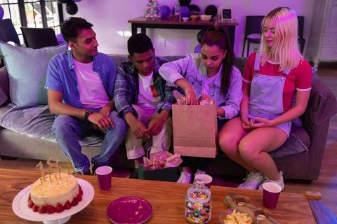Diverse friends unwrap birthday gifts, warm celebration at home