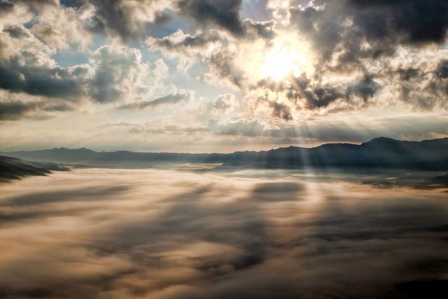 Vibrant depiction of a sunrise with sunbeams shining through clouds over misty mountains. Ideal for backgrounds, travel ads, inspirational quotes, and nature blogs.