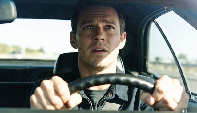 Tense adult male driving gripping steering wheel scanning highway with focused gaze