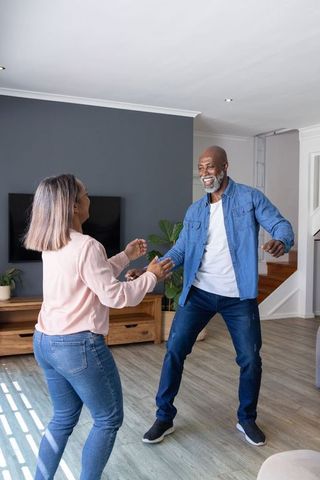 Diverse mature couple dancing together in sunlit modern living room