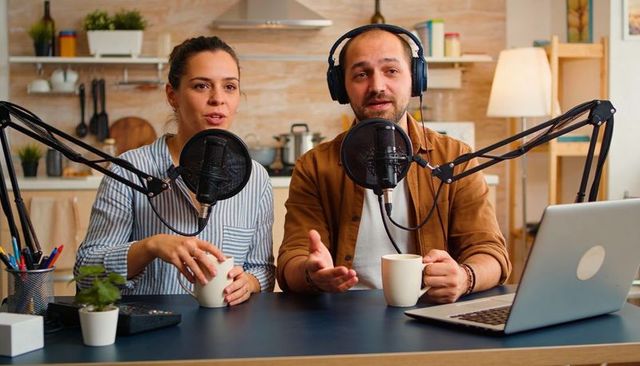 Podcast hosts recording conversational episode at home kitchen counter with microphones