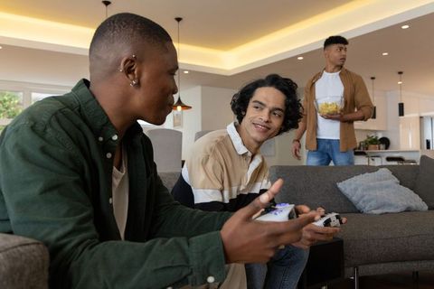 Diverse friends playing video games on sofa sharing snacks in modern apartment
