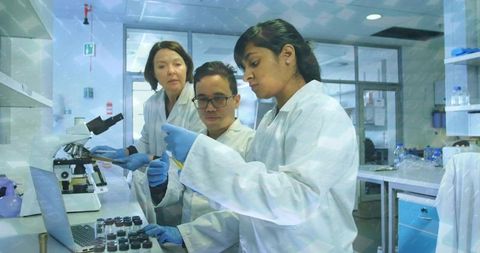 Lab team pipetting reagents at bench with laptop, microscope and vial rack for research
