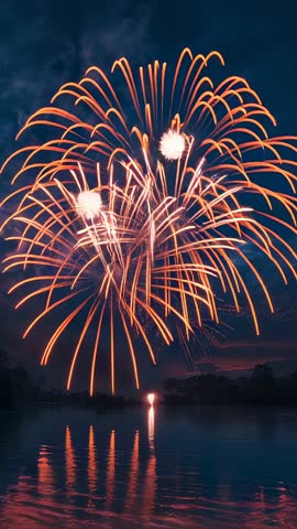 Vertical video showing golden fireworks bursting over lake at dusk with water reflection
