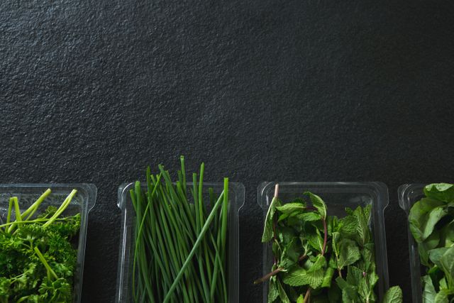 Fresh herbs in plastic trays on a dark background, showcasing chives, mint, and parsley. Ideal for use in culinary blogs, healthy eating articles, food preparation guides, and kitchen ingredient displays.