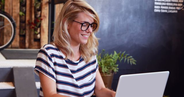 Smiling Woman with Glasses Working on Laptop in Modern Cafe - Download Free Stock Images Pikwizard.com