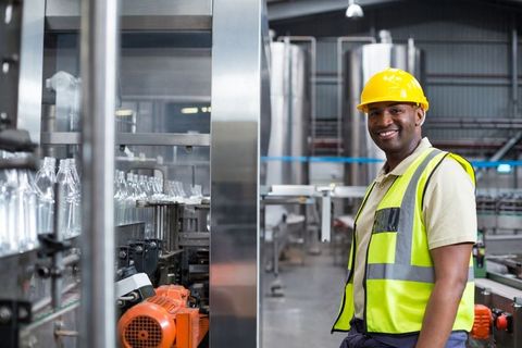 Factory worker inspecting bottles on conveyor in manufacturing plant