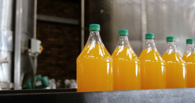 Row of five bottles with green tops containing orange juice. Food and drink industry concept.