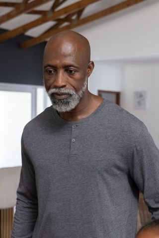 Senior african man standing indoors looking down with contemplative gaze, grey henley