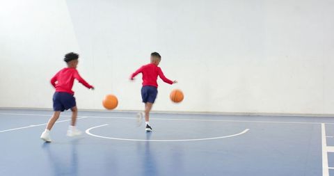 Energetic boys dribbling basketballs in indoor gym