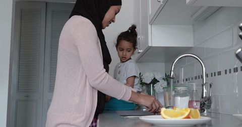 Mother in hijab and daughter in modern kitchen daily routine