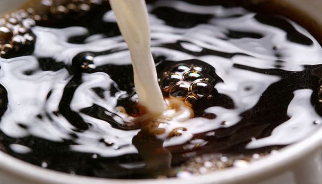Creamy milk pouring into dark coffee creating swirl and ripple macro closeup