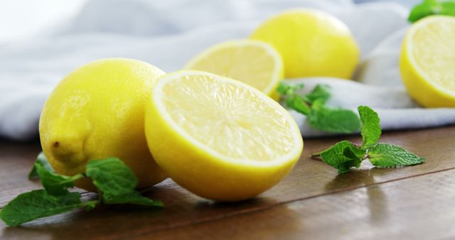 Lemons and mint leaves arranged on a rustic wooden surface create a vibrant and fresh look. Ideal for use in healthy eating and lifestyle blogs, recipe illustrations, kitchen decor, and food product advertisements.