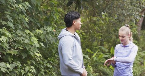 Couple checking smartwatch on wooded trail wearing activewear and planning outdoor run