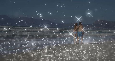 Couple strolling along moonlit beach at dusk with sparkling bokeh and coastal silhouette