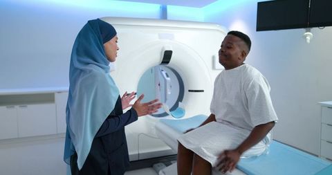 Multicultural clinician in hijab explaining ct scan to patient on scanner table in hospital