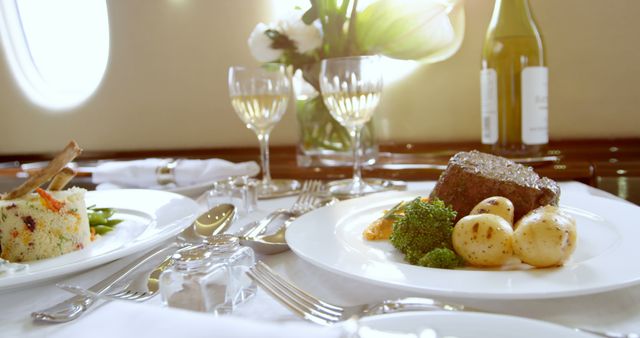 Private jet dining table featuring gourmet meal with steak, potatoes, broccoli, and wine. Luxury travel and upscale dining experience perfect for illustrating opulence and high-end travel services. Useful for articles, brochures, and advertisements targeting affluent travelers.