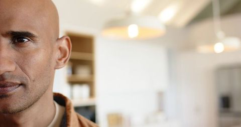 Bald man gazing in modern kitchen with warm pendant lights, thoughtful closeup portrait
