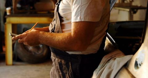 Mechanic Writing Work Order on Notepad while Holding Pencil in Greasy Garage Workshop