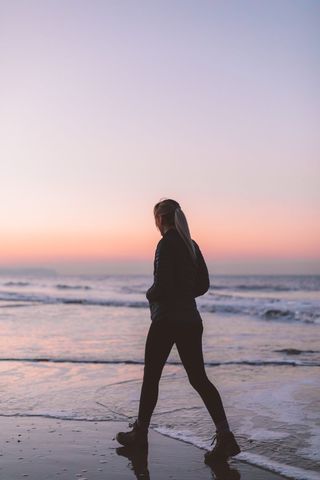 Woman Walking Along Seashore During Tranquil Sunset