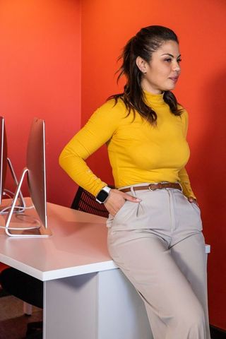 Professional woman leaning on desk wearing mustard turtleneck and smartwatch in modern office