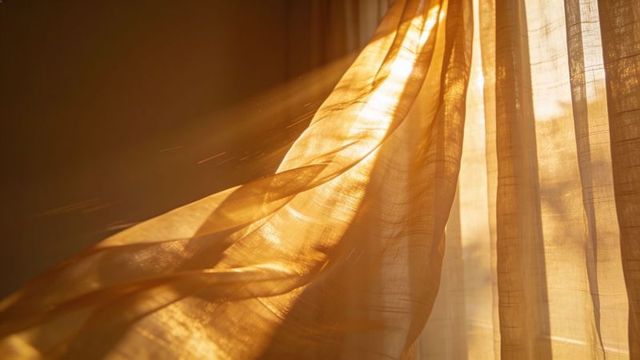 Golden sheer curtain billowing in sunlight with dust motes and textured pleats