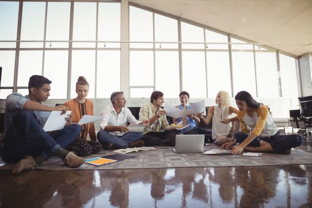 Group of creative business people sitting on the floor engaged in a collaborative work session. Ideal for illustrating modern workplace culture, teamwork, innovative business practices, and startup environments.