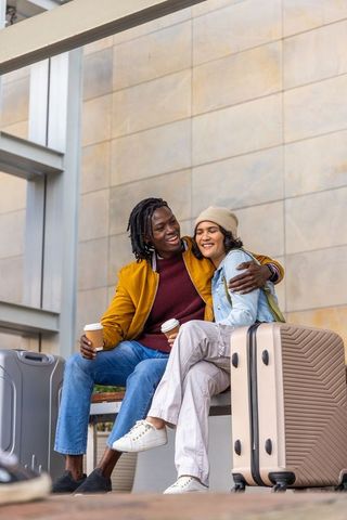 Young couple laughing and embracing at transit terminal with luggage and coffee