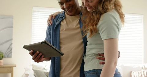 Young couple embracing while browsing tablet in bright sunlit contemporary living room