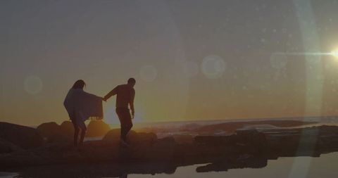 Couple Walking Along Rocky Shoreline at Tranquil Sunset