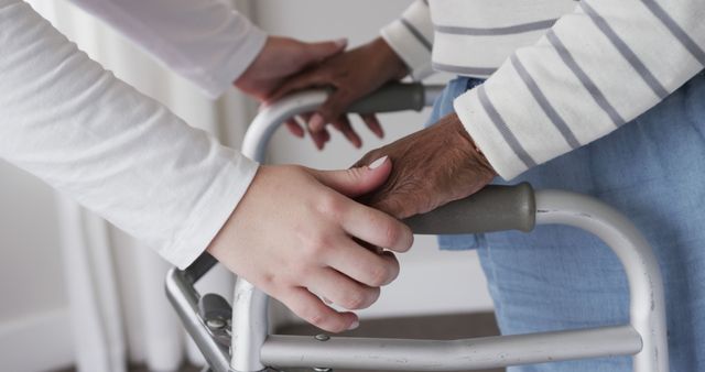 Caregiver holding hands with an elderly person using a walker, offering support and assistance. This image can be used for healthcare and caregiving themes, illustrating support for the elderly and promoting services for senior care.