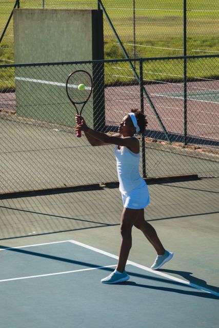 Full length of african american young female tennis player serving at court on sunny day. unaltered, sport, competition and tennis game concept.