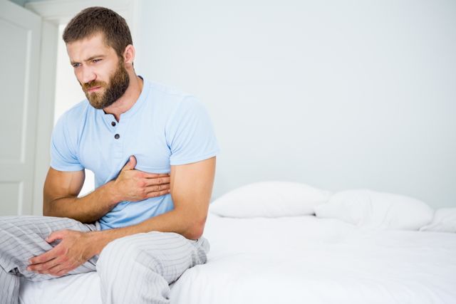 Young man having chest pain on bed in bedroom