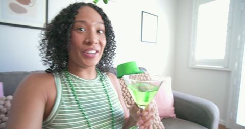 African american woman celebrating st patrick's day at home holding neon green cocktail