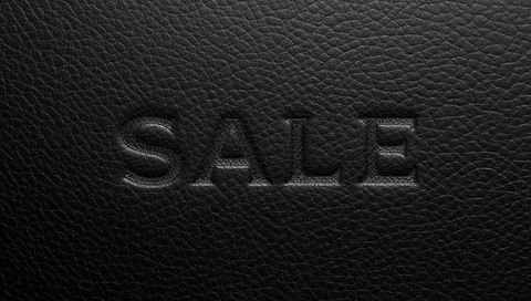 Embossed sale lettering on black leather texture creating luxurious minimalist retail visual
