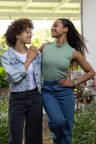 Smiling african american friends embracing on sunlit porch with garden plants in denim