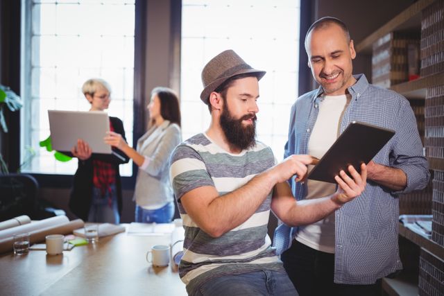 Male coworkers smiling while discussing over digital tablet in creative office