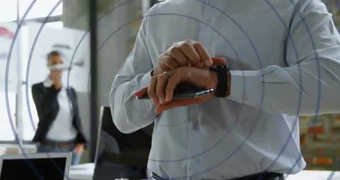 Executive tapping smartwatch while lowering smartphone in modern open-plan office