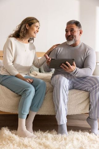 Mature couple relaxing on bed using tablet, cozy home lifestyle morning