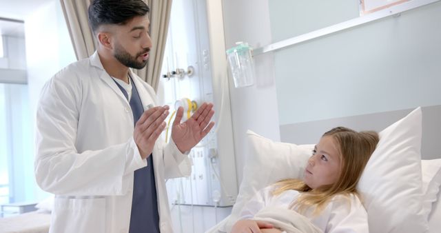 Diverse male doctor with asthma inhaler explaining to girl patient in hospital bed. Consultation, treatment, childhood, illness, medical services, healthcare and hospital, unaltered.