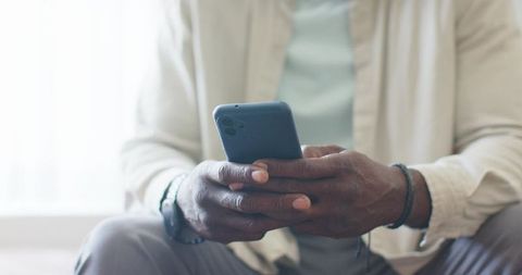 Mature african american man holding smartphone by window in casual beige shirt with watch visible