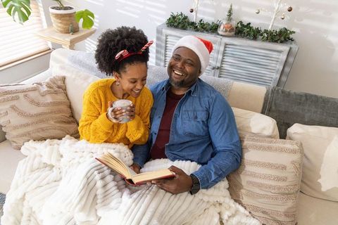 African American Couple Enjoying Cozy Christmas Morning on Sofa with Blanket and Book