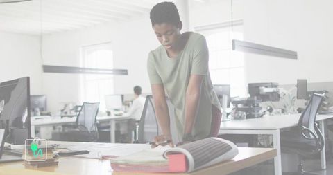 Team lead reviewing plans leaning over desk in modern open office with color-coded binder