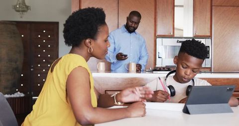 African American family sharing morning routine in kitchen while child studying on tablet