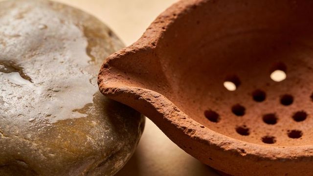 Perforated terracotta strainer featuring weathered river stone on warm surface