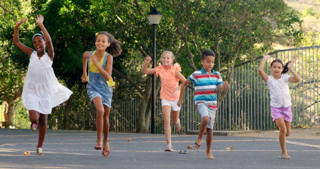 A diverse group of children is running and playing joyfully on a tree-lined street under a clear sky. The image captures a sense of fun and active lifestyle, ideal for promoting outdoor activities, childhood happiness, and friendship. Suitable for use in advertisements for summer camps, playgrounds, or healthy living campaigns.