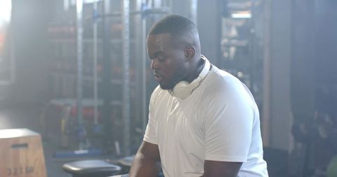 African man catching breath after intense weightlifting session in gym with headphones